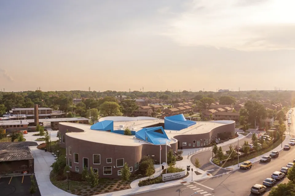 A large, multi-use building is adorned with blue canopies, pictured in the sunset of an urban landscape.